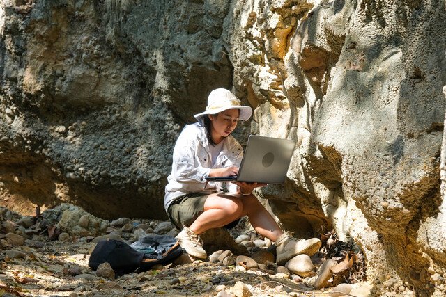 Field researcher using a laptop beside a rock outcrop